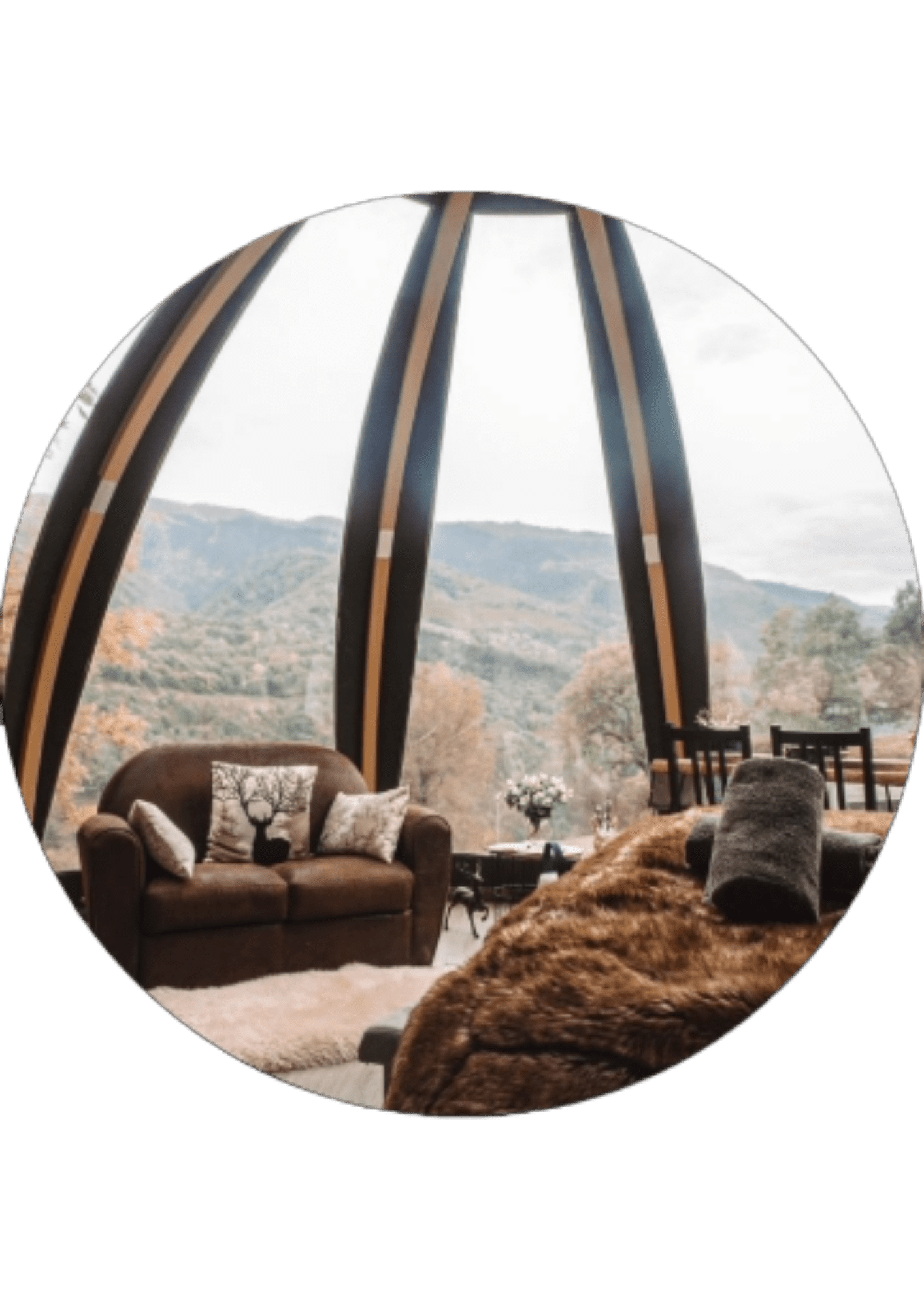 A cozy room with a brown sofa, a bed with a fur blanket and panoramic windows overlooking to the mountains and forest