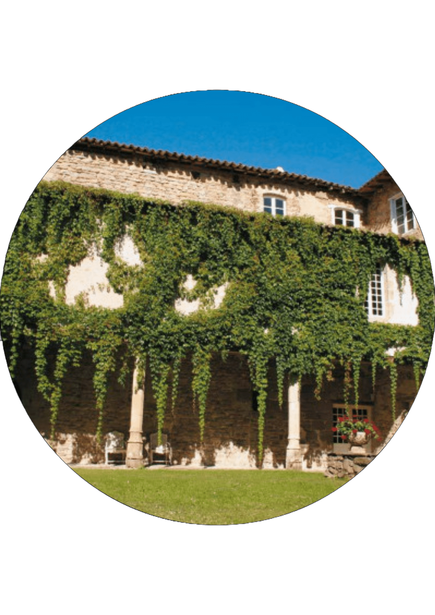 A stone courtyard featuring a lush green lawn and an ancient building facade under a bright blue sky
